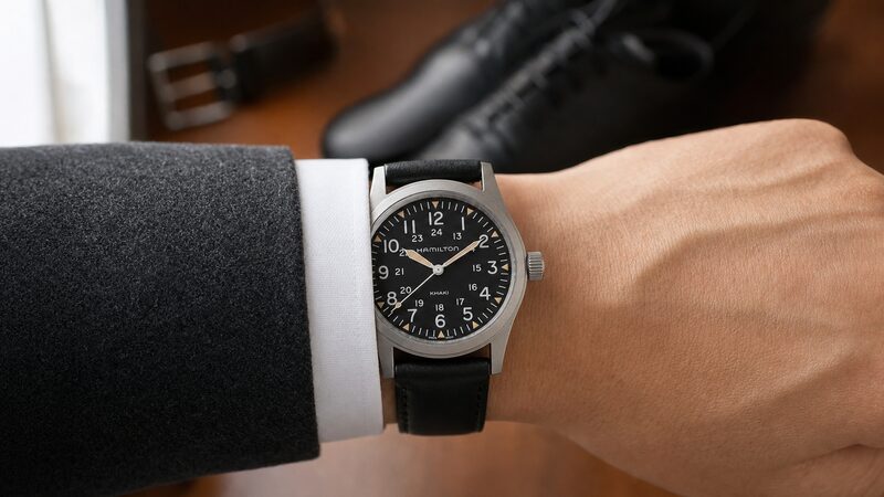 黒レザー20mmを装着したカーキ フィールド メカニカル38mmが白いドレスシャツのカフスの下へ収まる様子を手首から下だけで写した実践カット