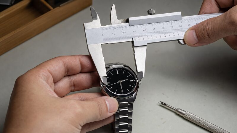 ラグ幅を測るノギスとバネ棒外し工具を時計のラグに当て、サイズ間違いと破損リスクを示す接写イメージ
