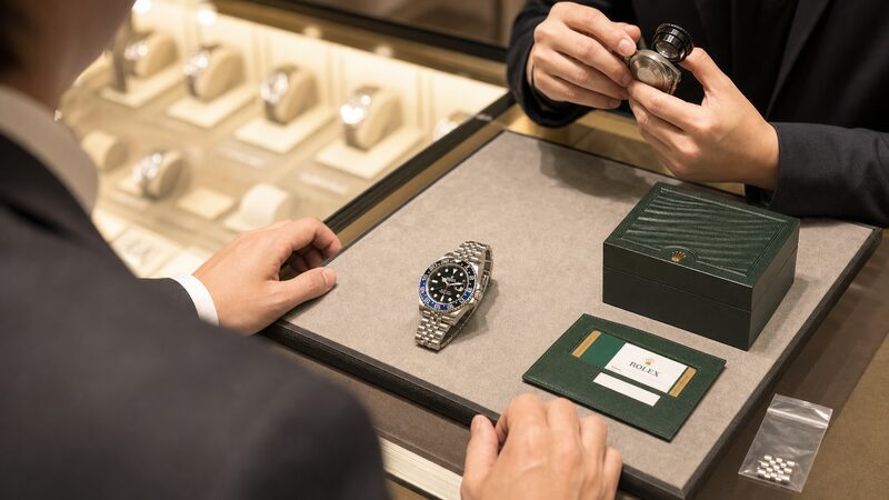 査定カウンターに置かれたバットマンと保証書・箱・予備コマ。売却時の相場と査定のコツを示す実践場面の写真
